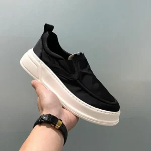 Chaussure slip-on homme noire tenue à la main avec semelle blanche confortable